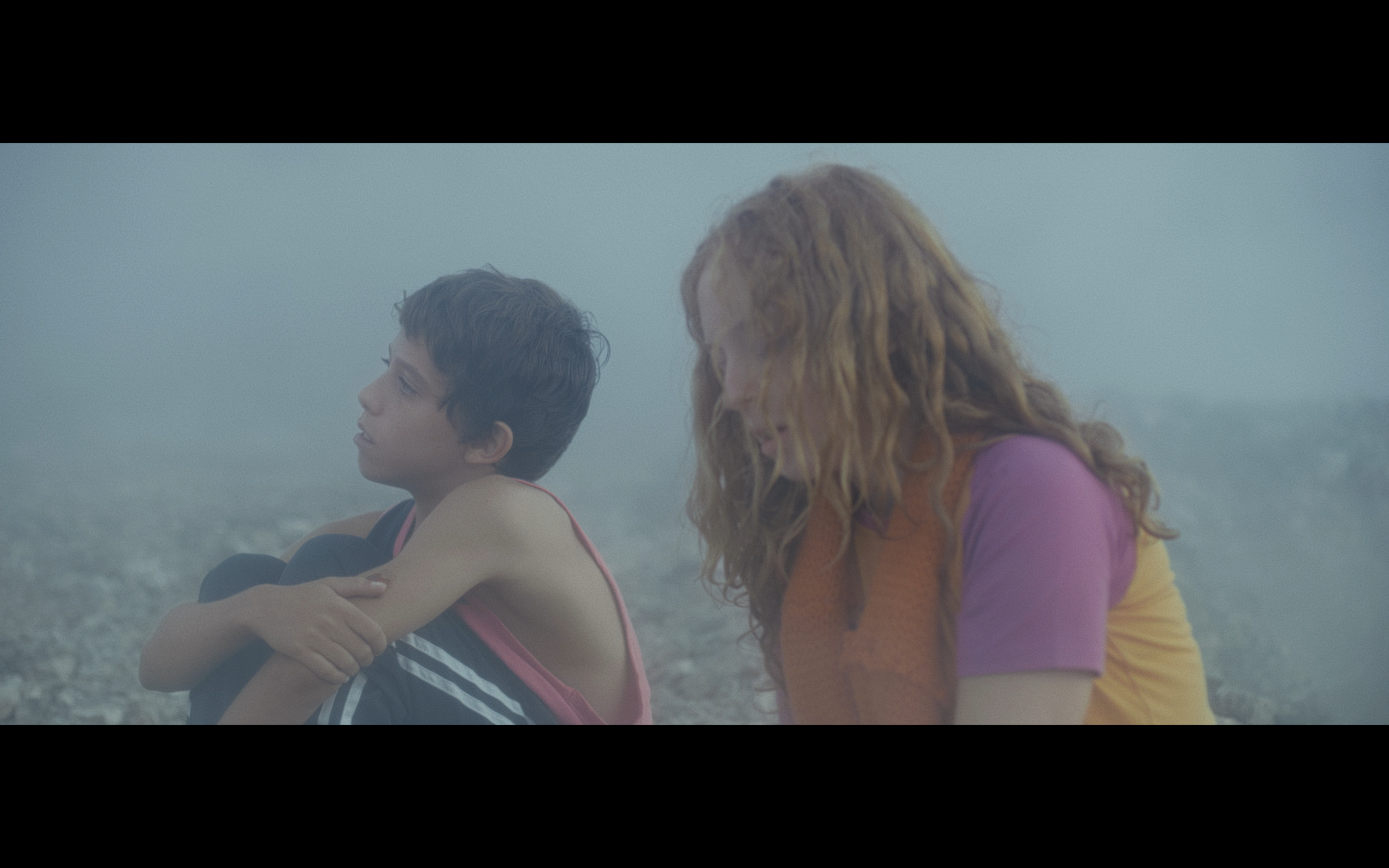 Two children sitting beside the sea in mist