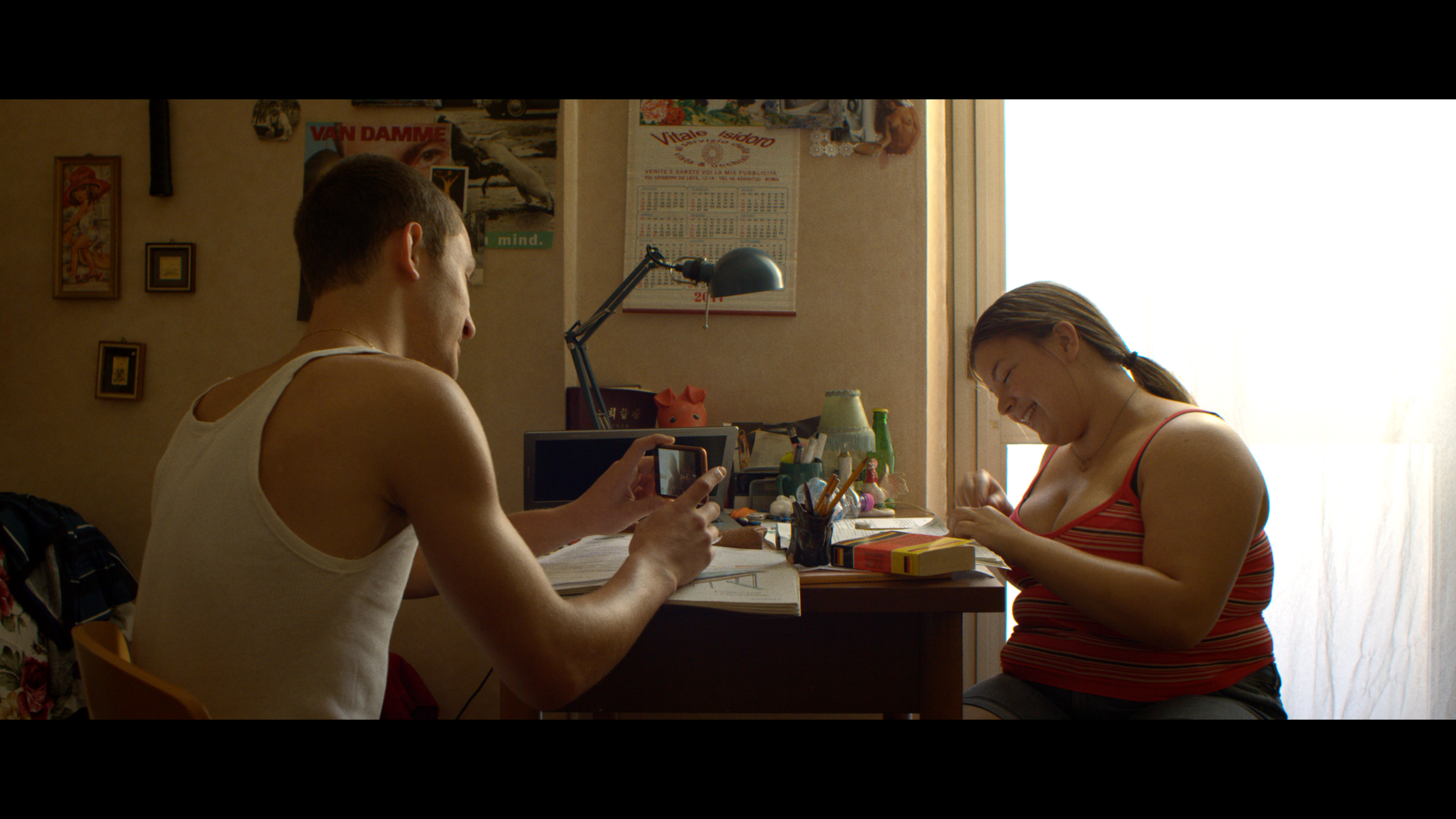 A young man filming a woman in a sunlit bedroom