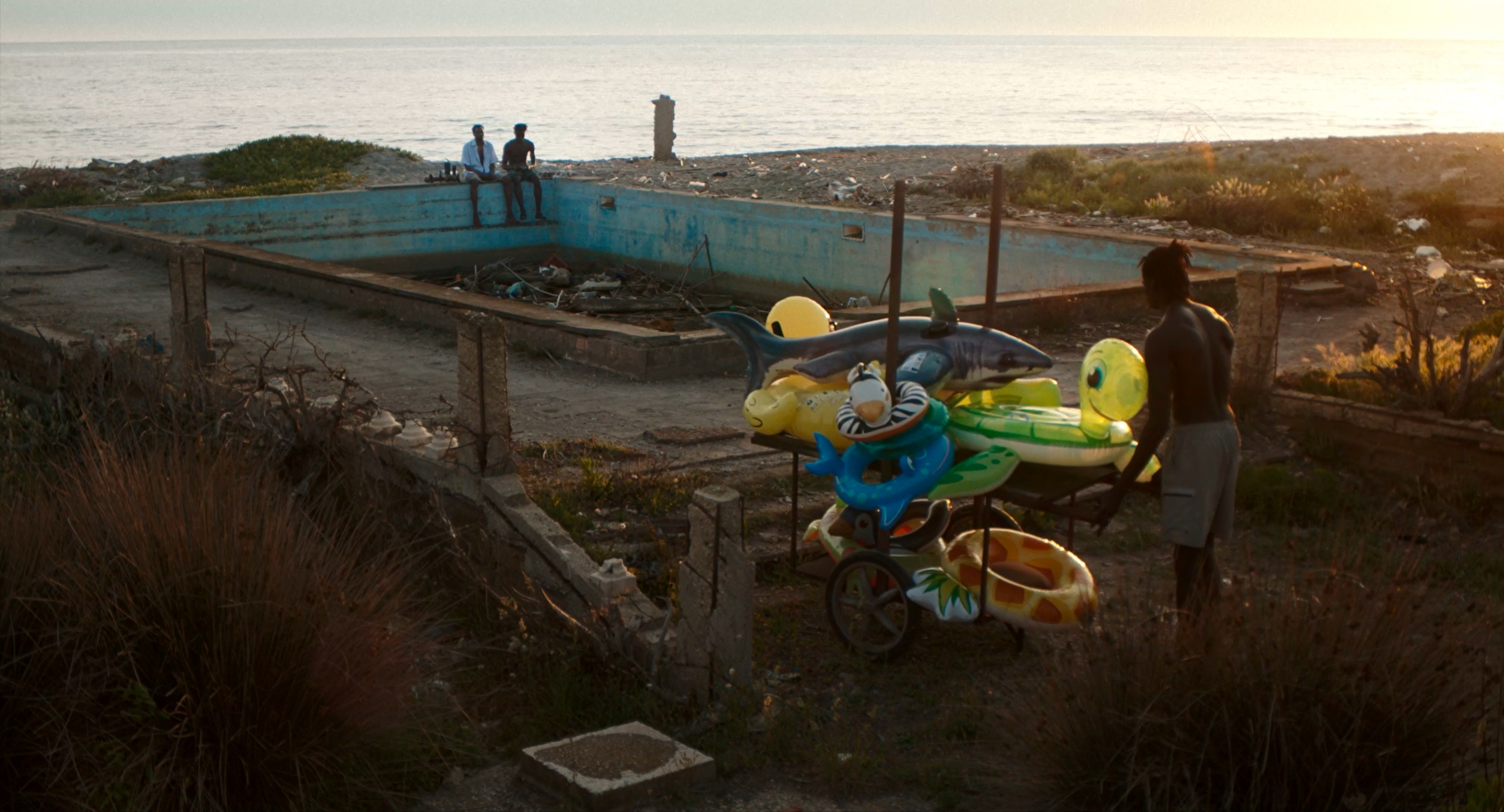 A man with inflatable beach toys beside an abandoned swimming pool