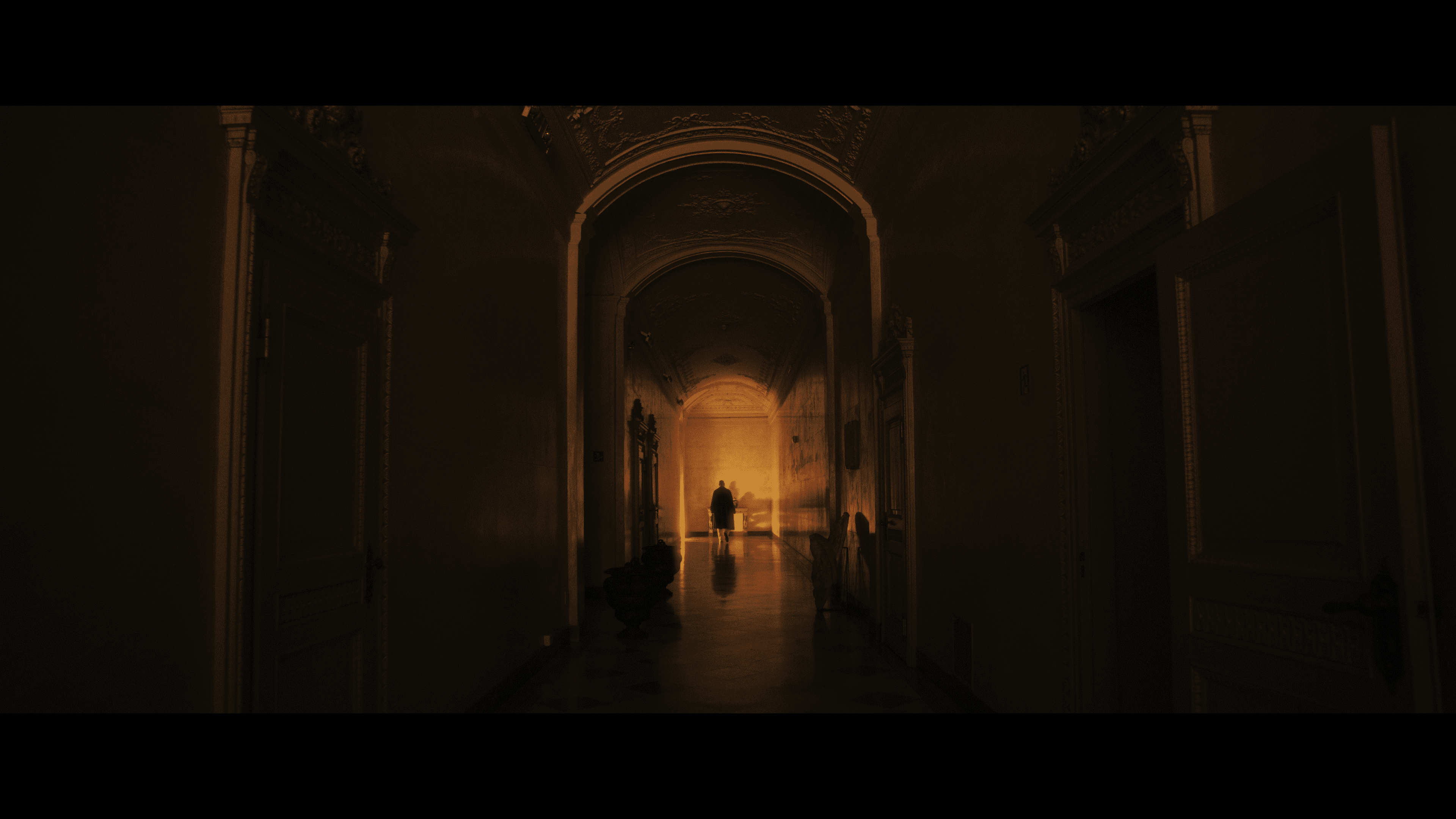 A figure at the end of a grand corridor in golden light