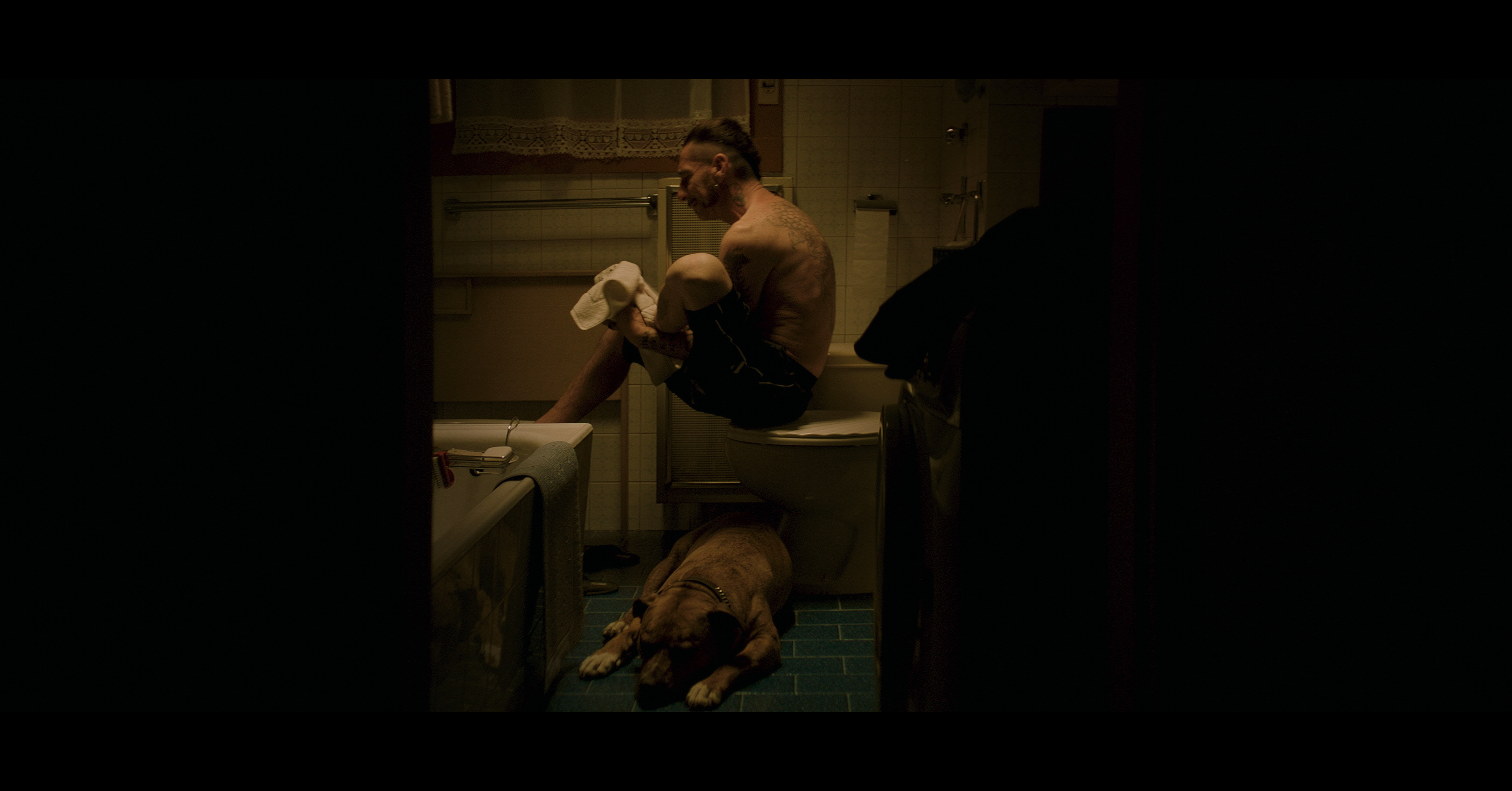 A man sitting in a bathroom with a dog at his feet