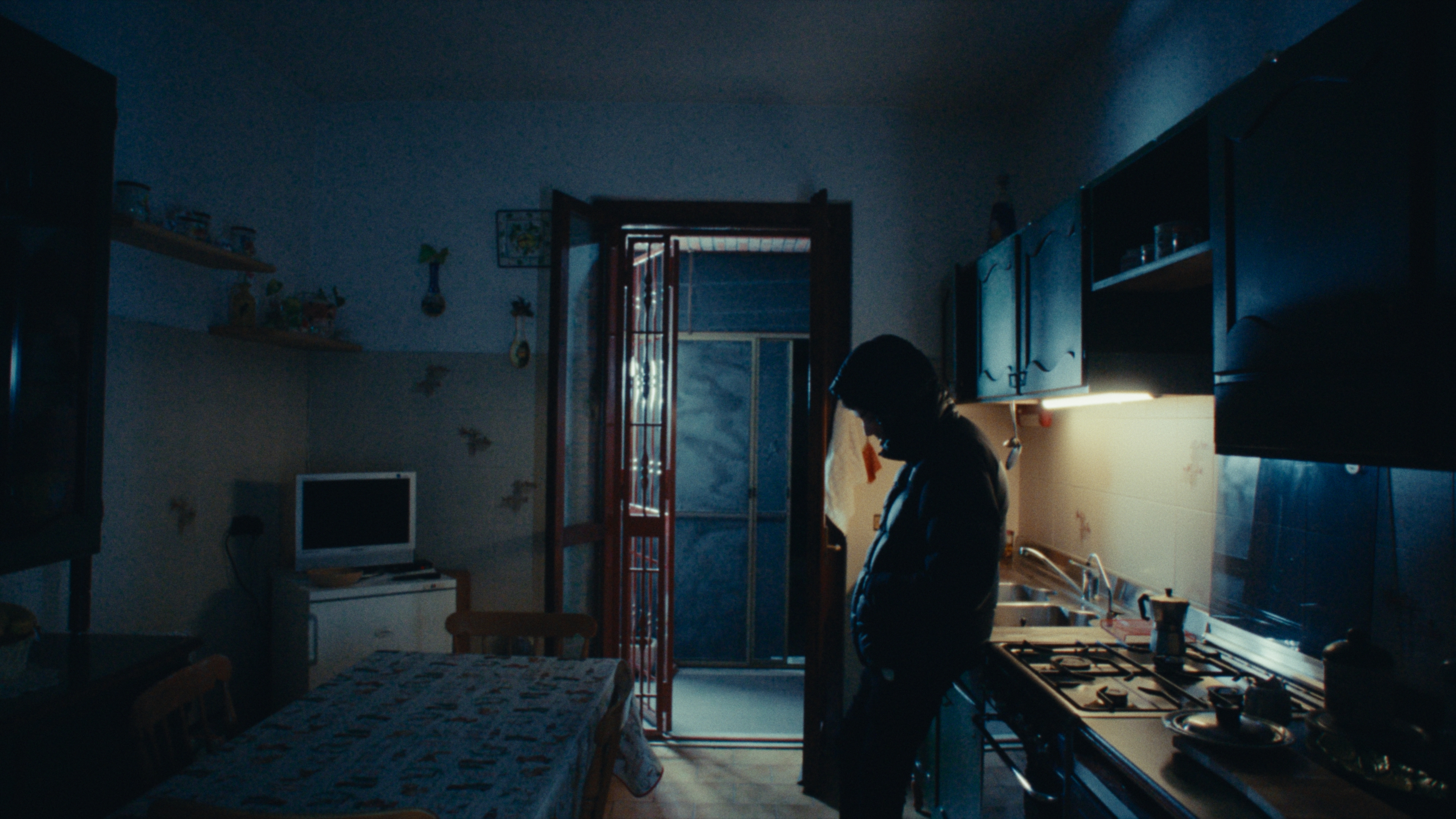 A hooded figure in a kitchen in cool blue light
