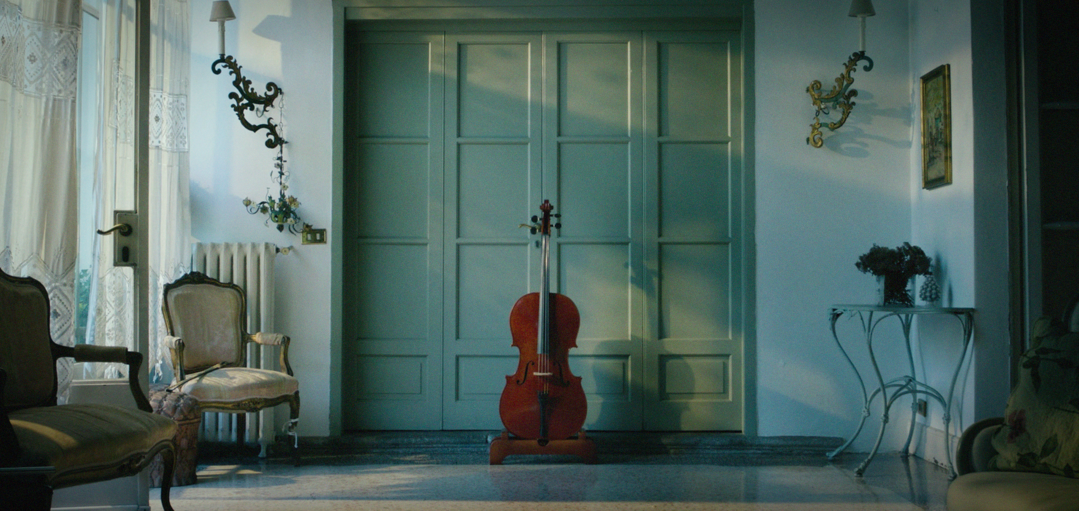 A cello beside antique chairs and a sunlit window