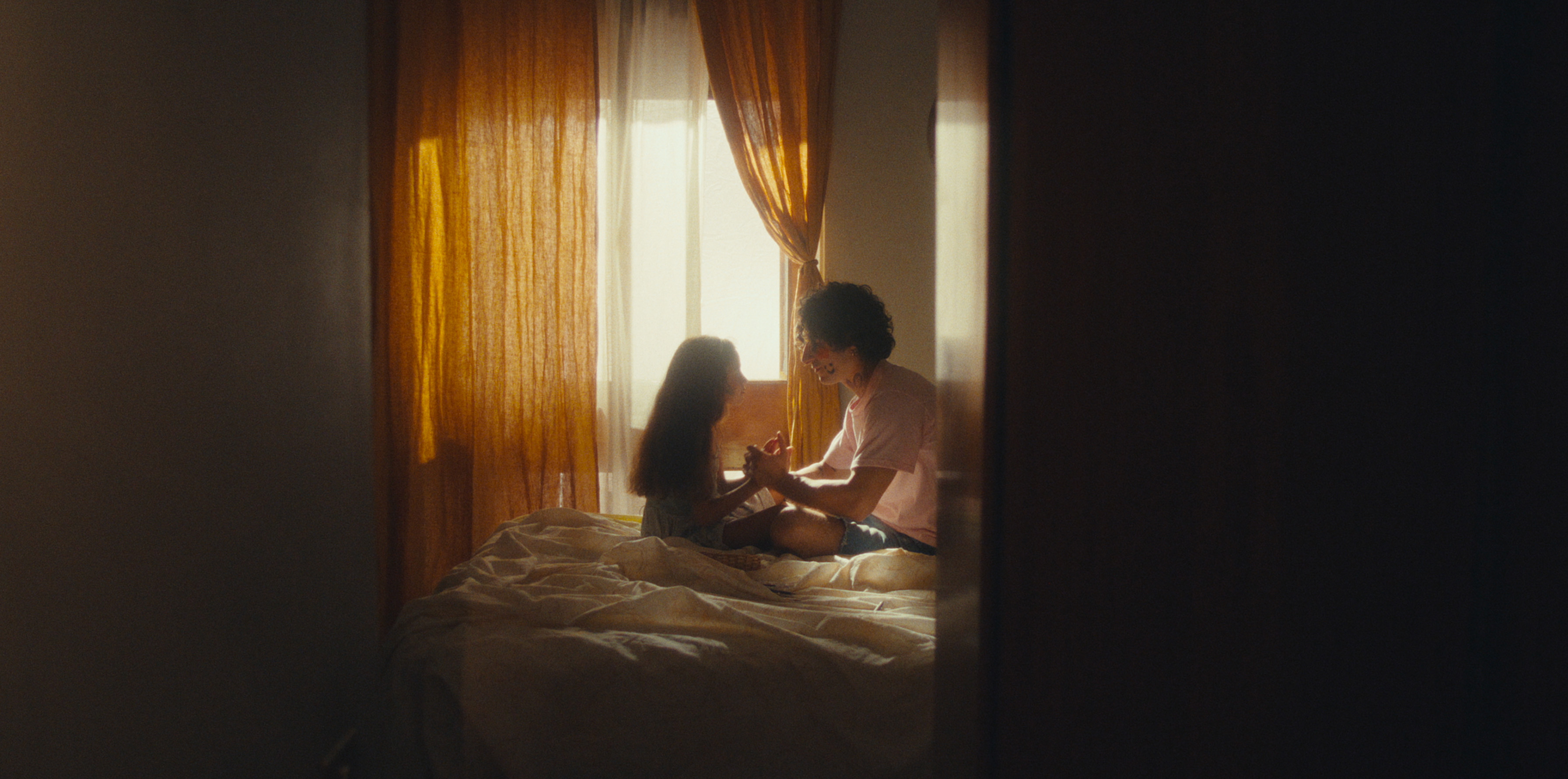 A child and an adult sitting on a bed by a sunlit window