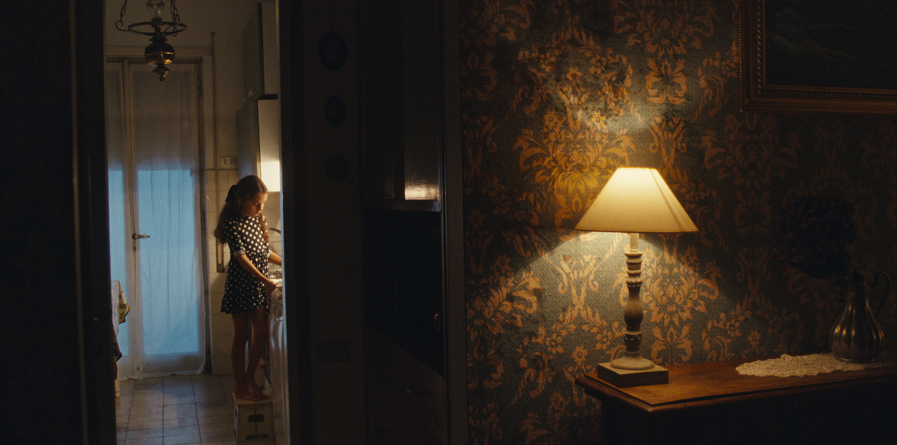 A child seen through a doorway beside a warmly lit room