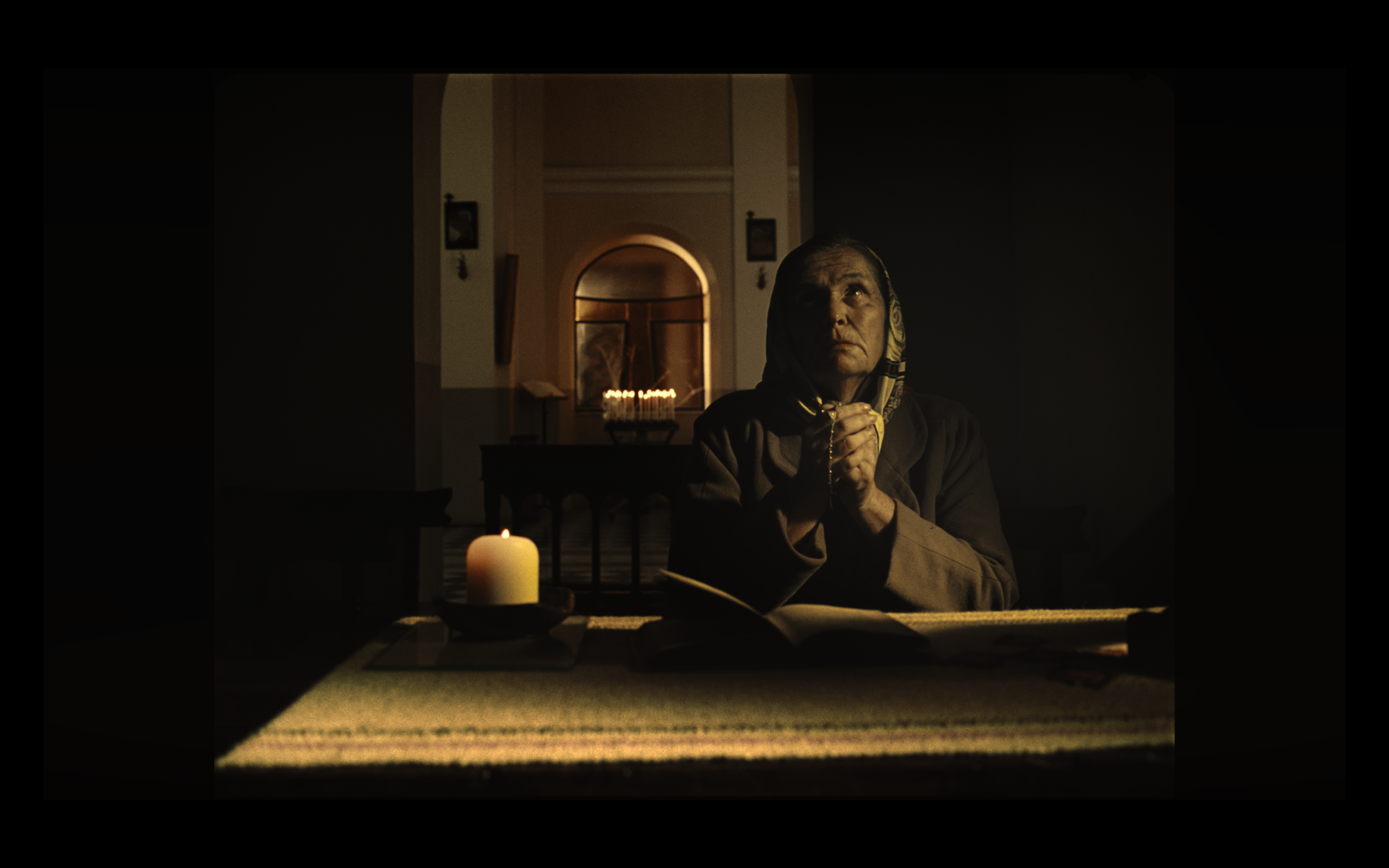 An older woman praying beside a candle in a church