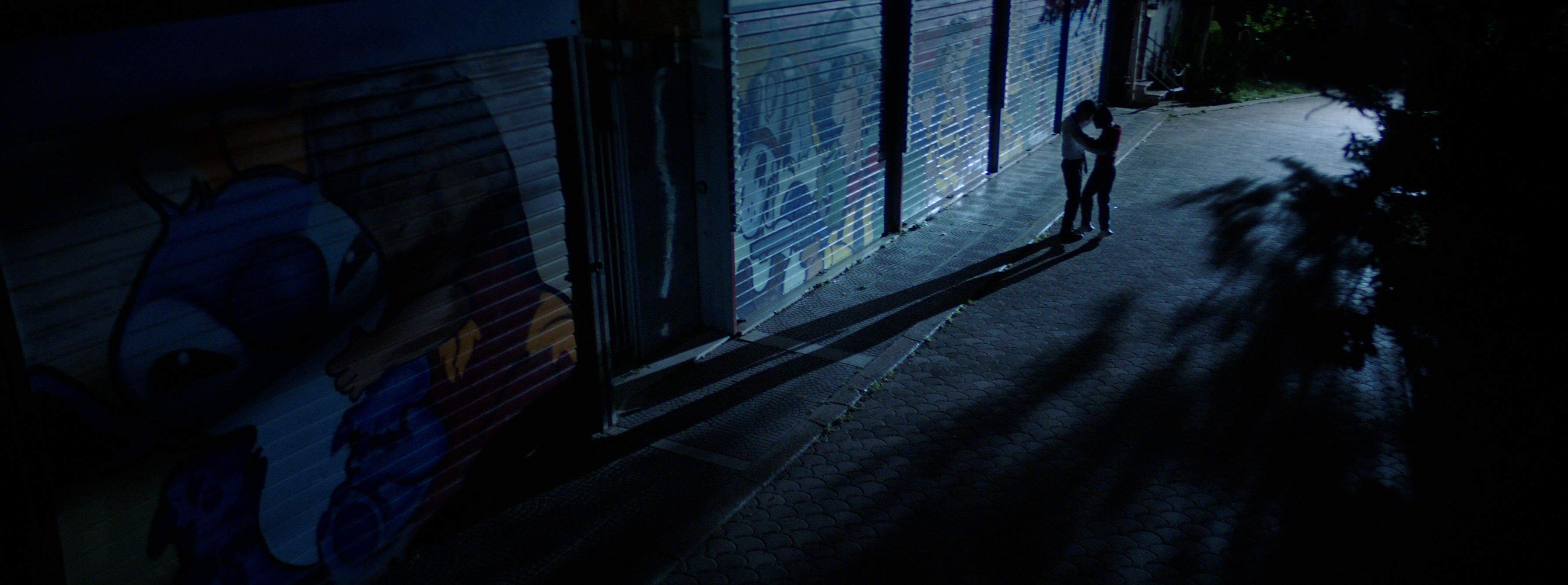A couple embracing on a blue-lit street at night