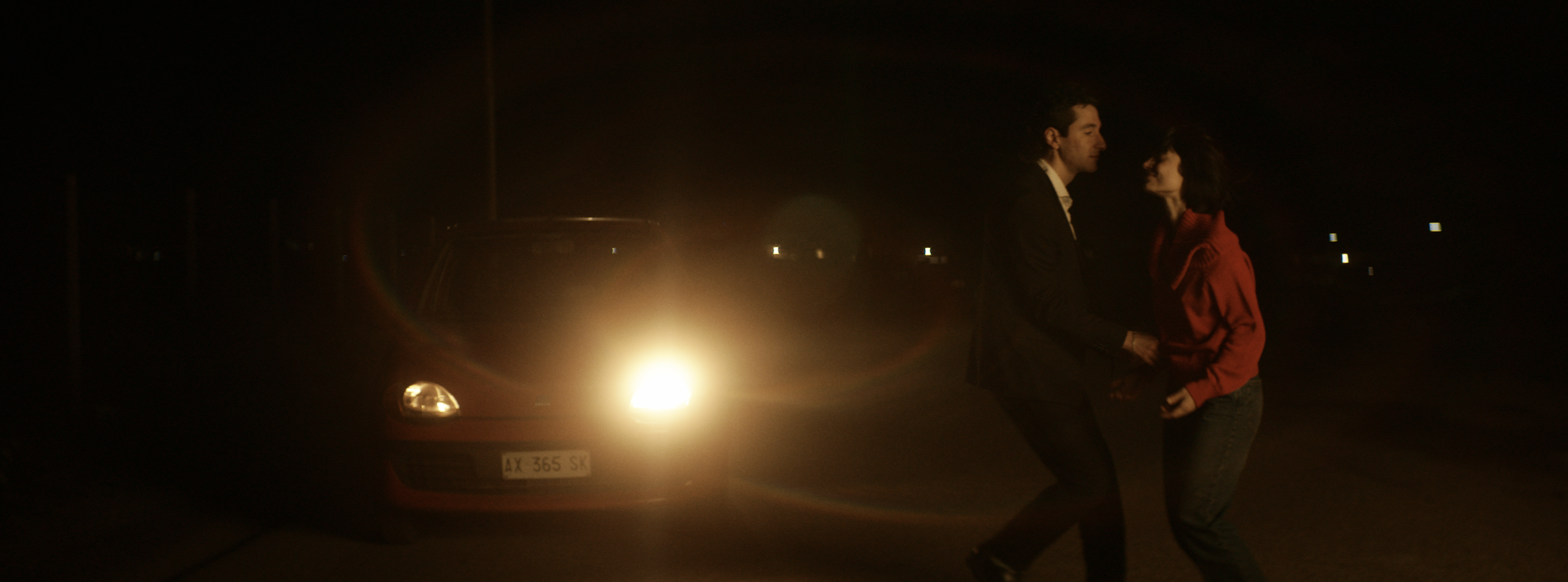A couple dancing beside a car in warm headlights