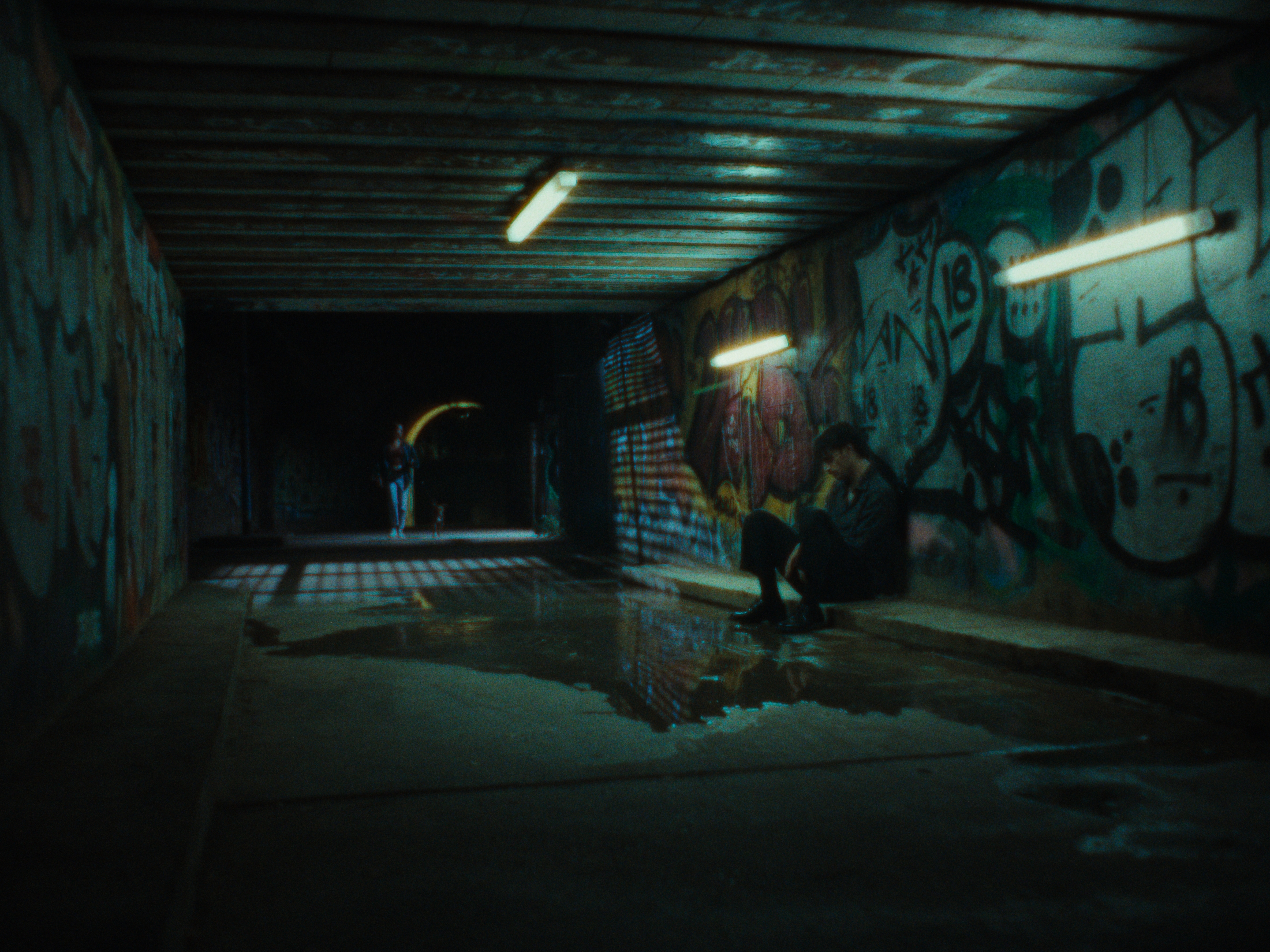 A figure sitting in a fluorescent-lit underpass