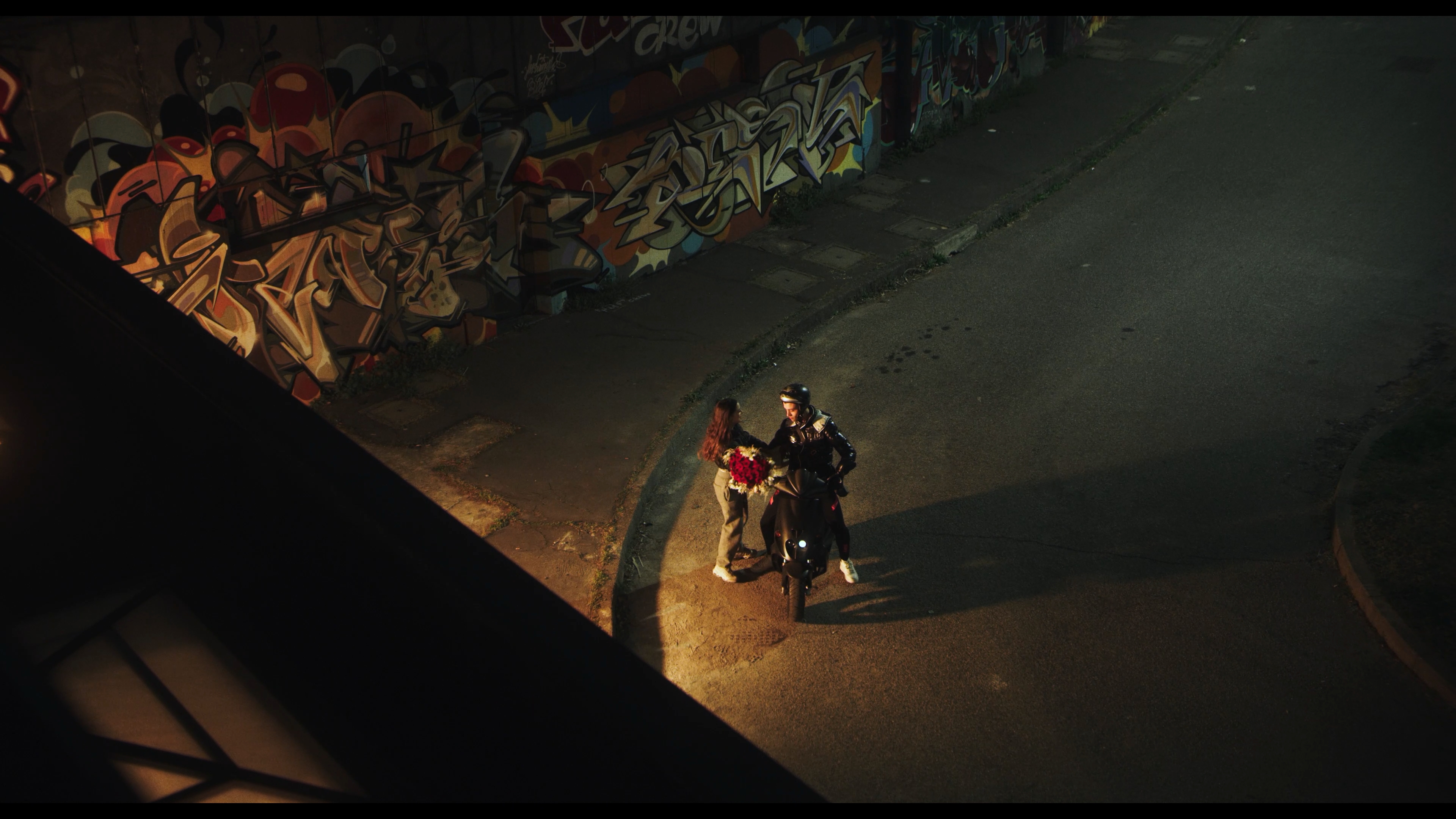 A couple beside a scooter beneath a graffiti-covered wall
