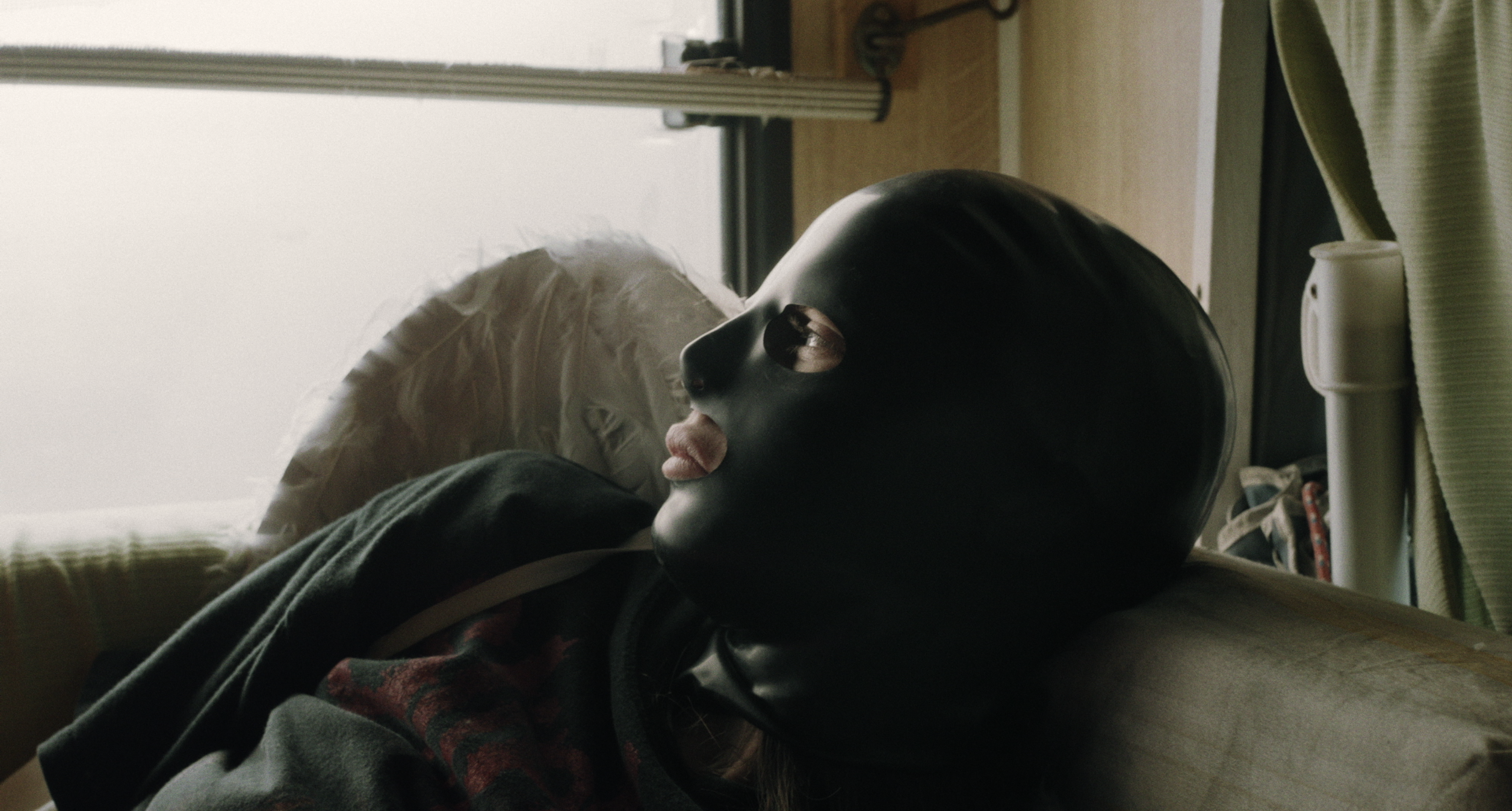 A person wearing a black mask beside a softly lit window