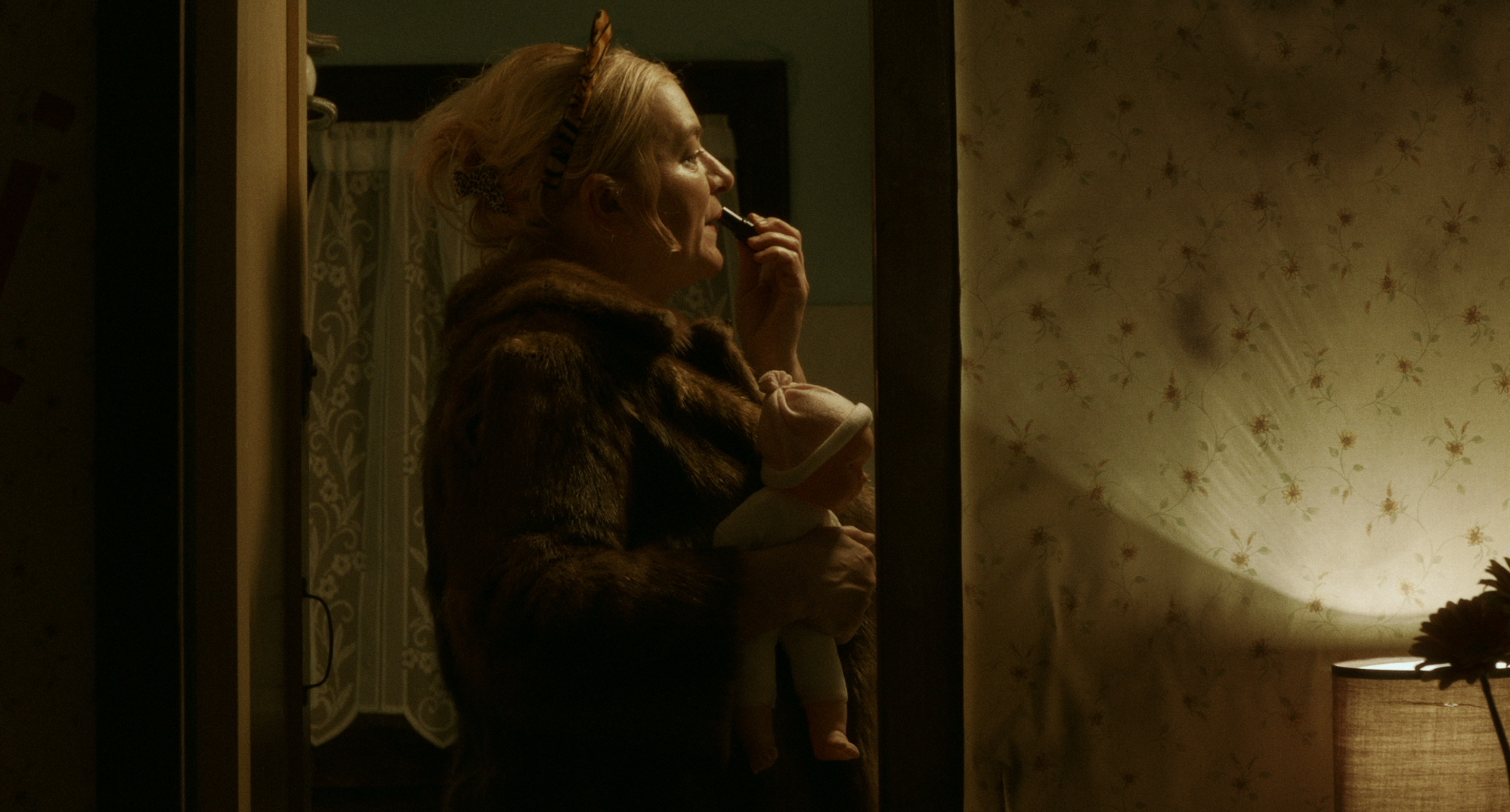 A woman applying lipstick beside a mirror in warm light