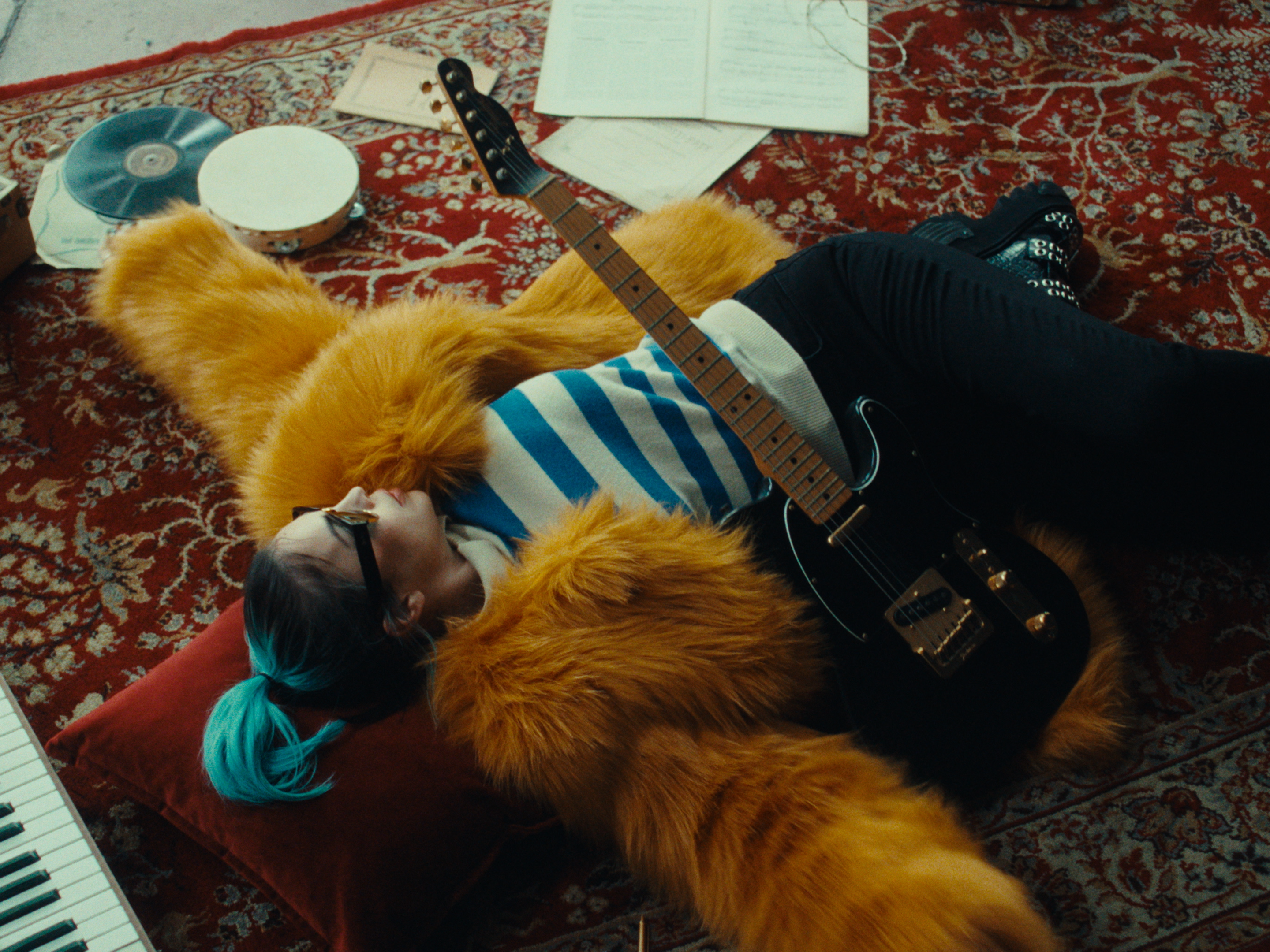 A woman lying on a patterned rug with a guitar
