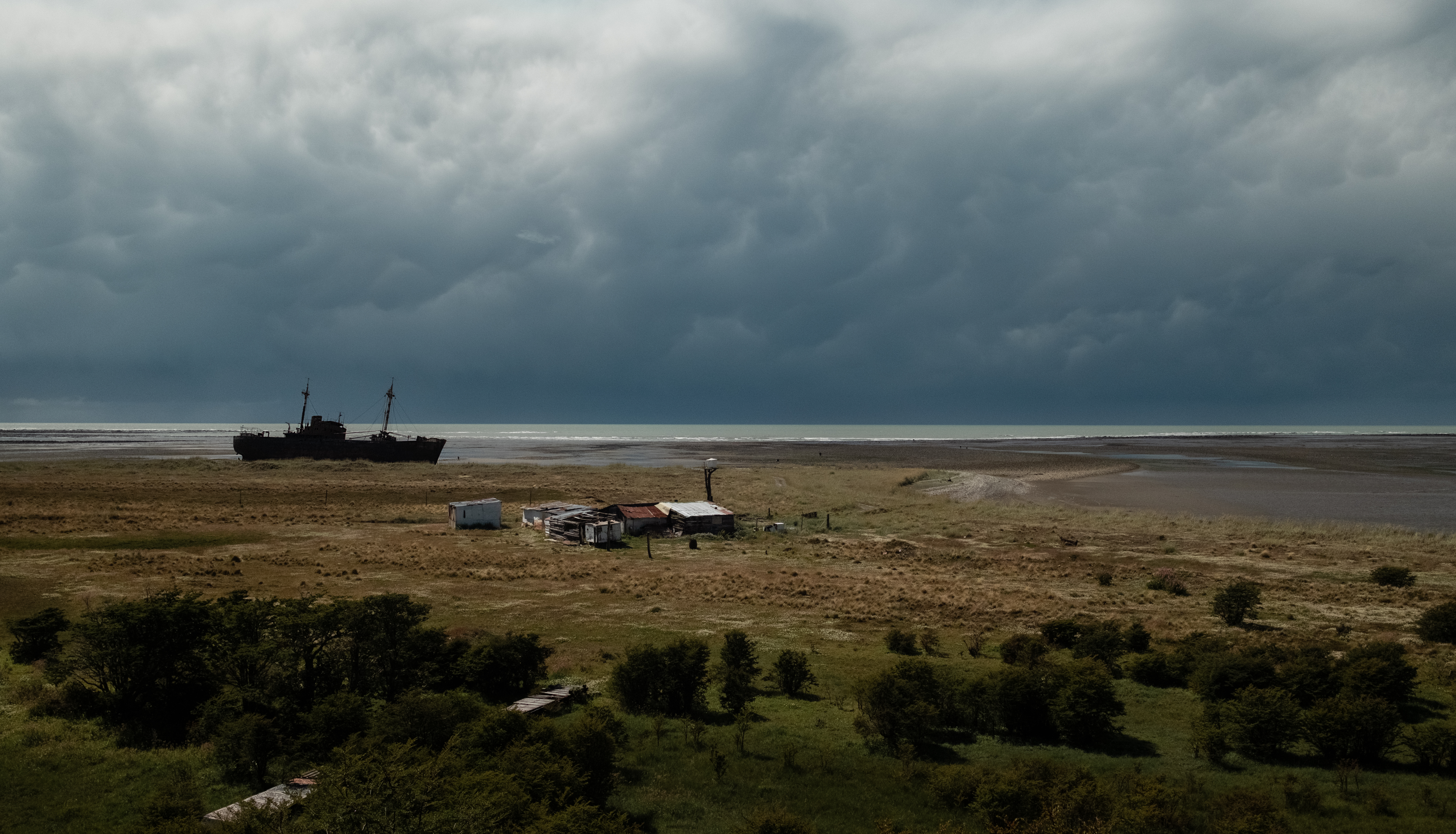 A shipwreck on a broad shoreline beneath storm clouds