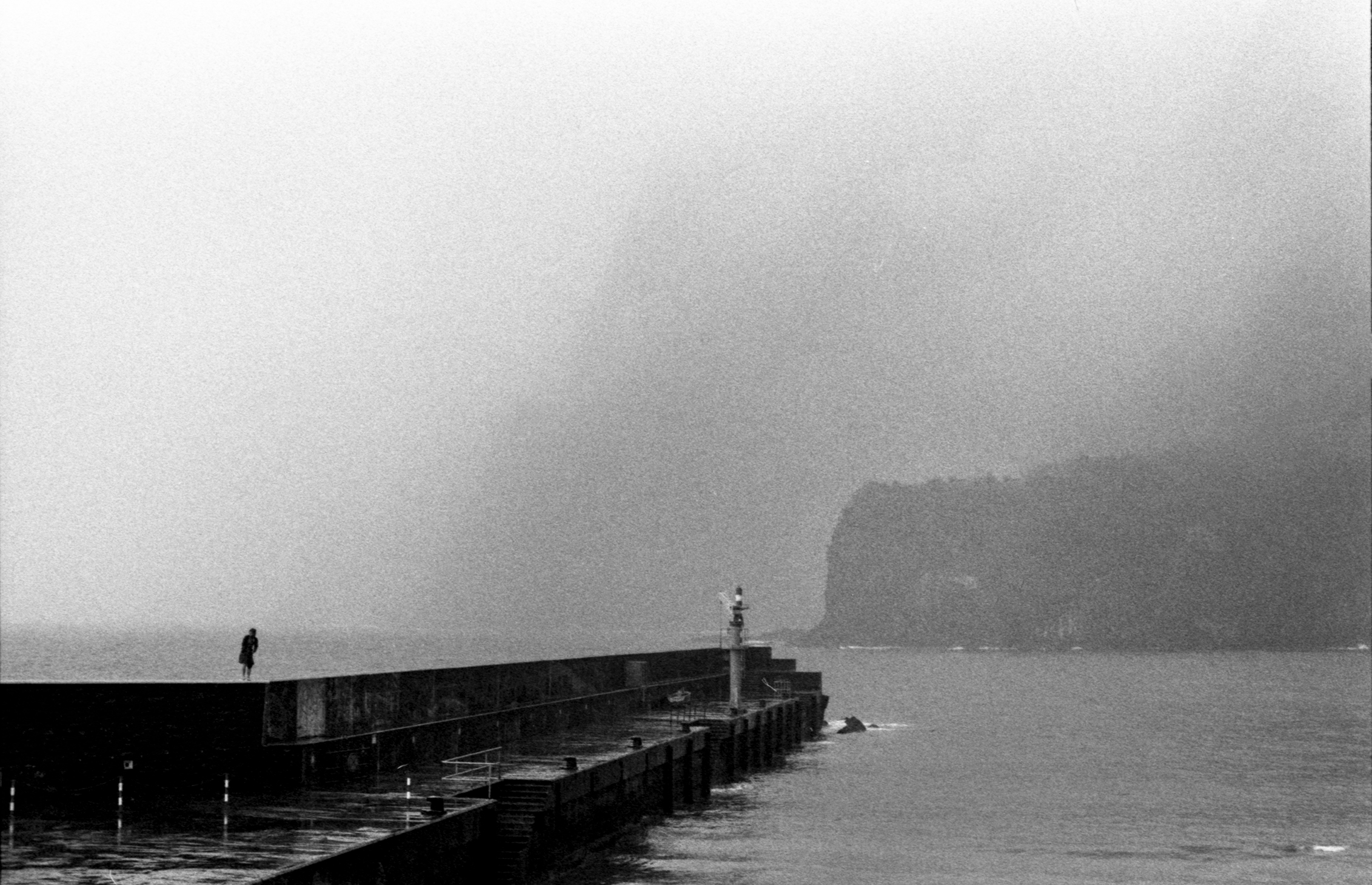 A lone figure on a pier beneath mist-covered cliffs