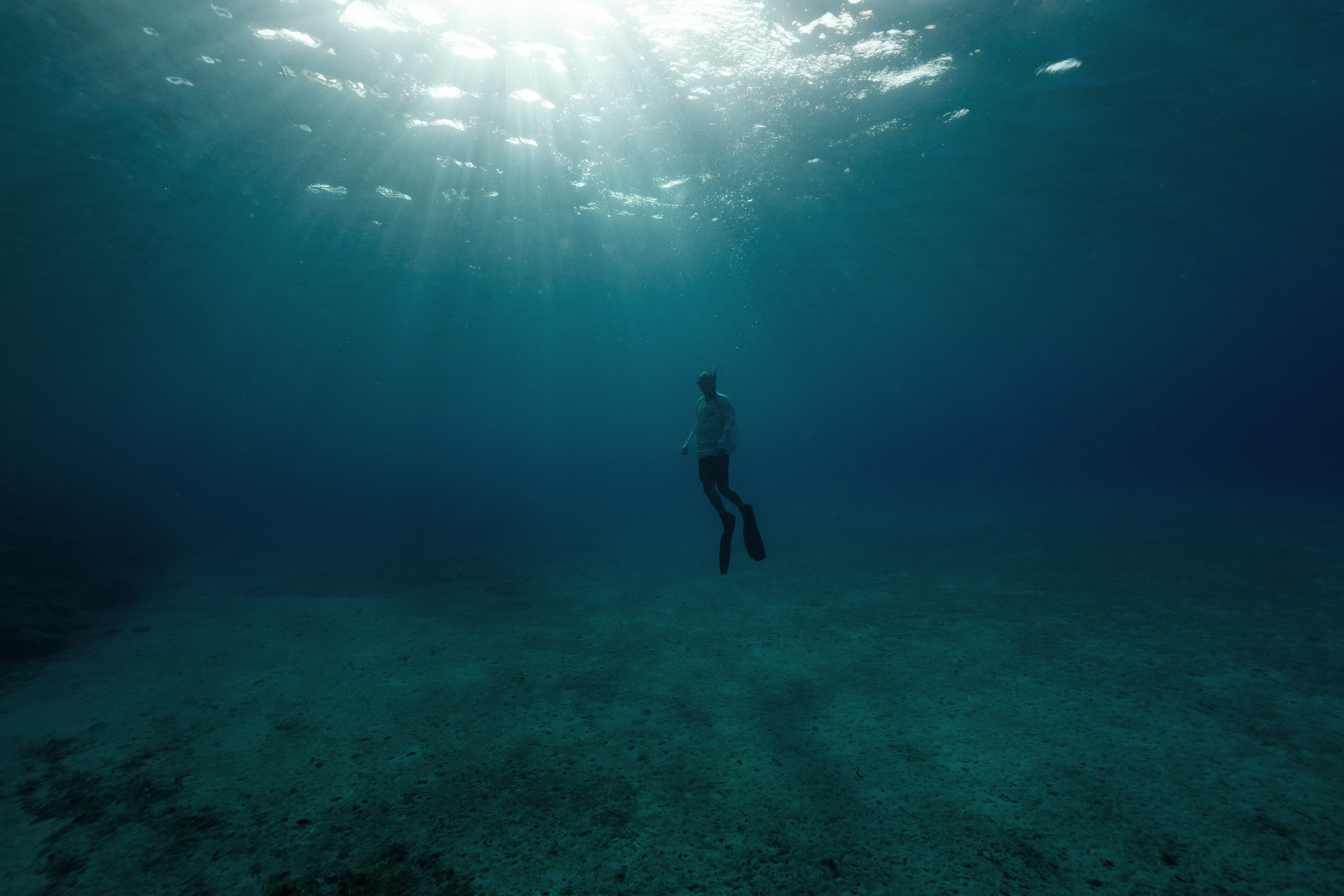 A swimmer suspended beneath rays of sunlight underwater