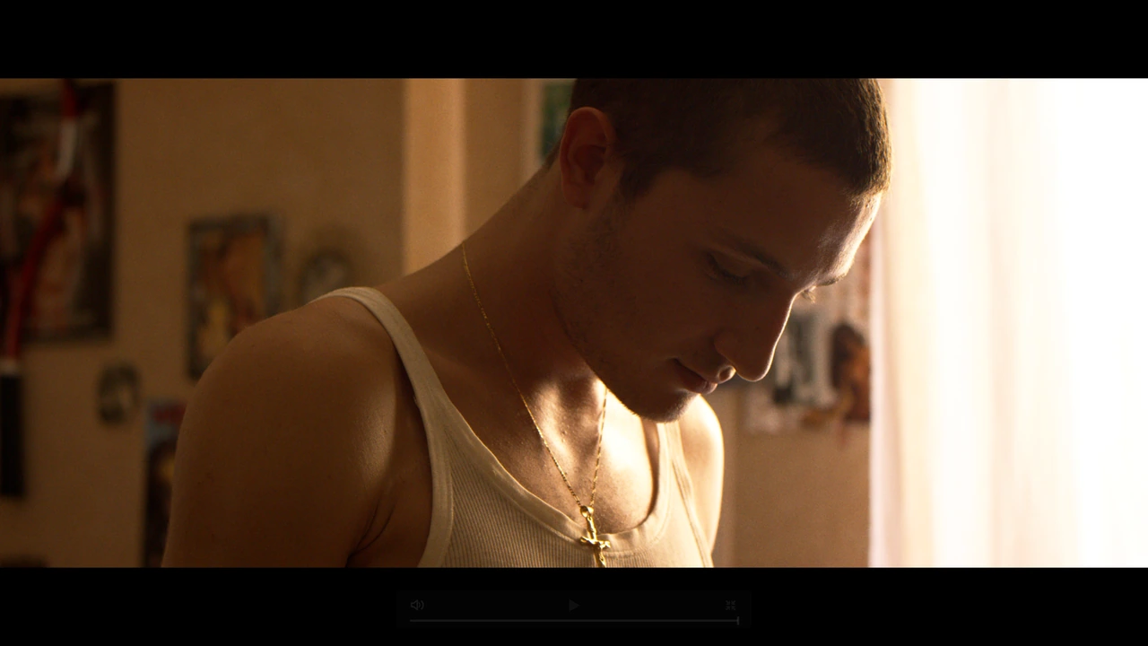 A young man looking down beside a bright window