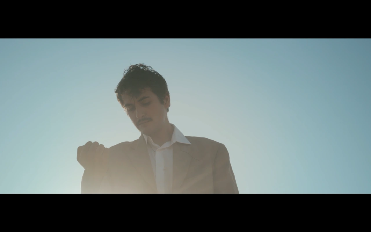 A man looking at his hand beneath a blue sky