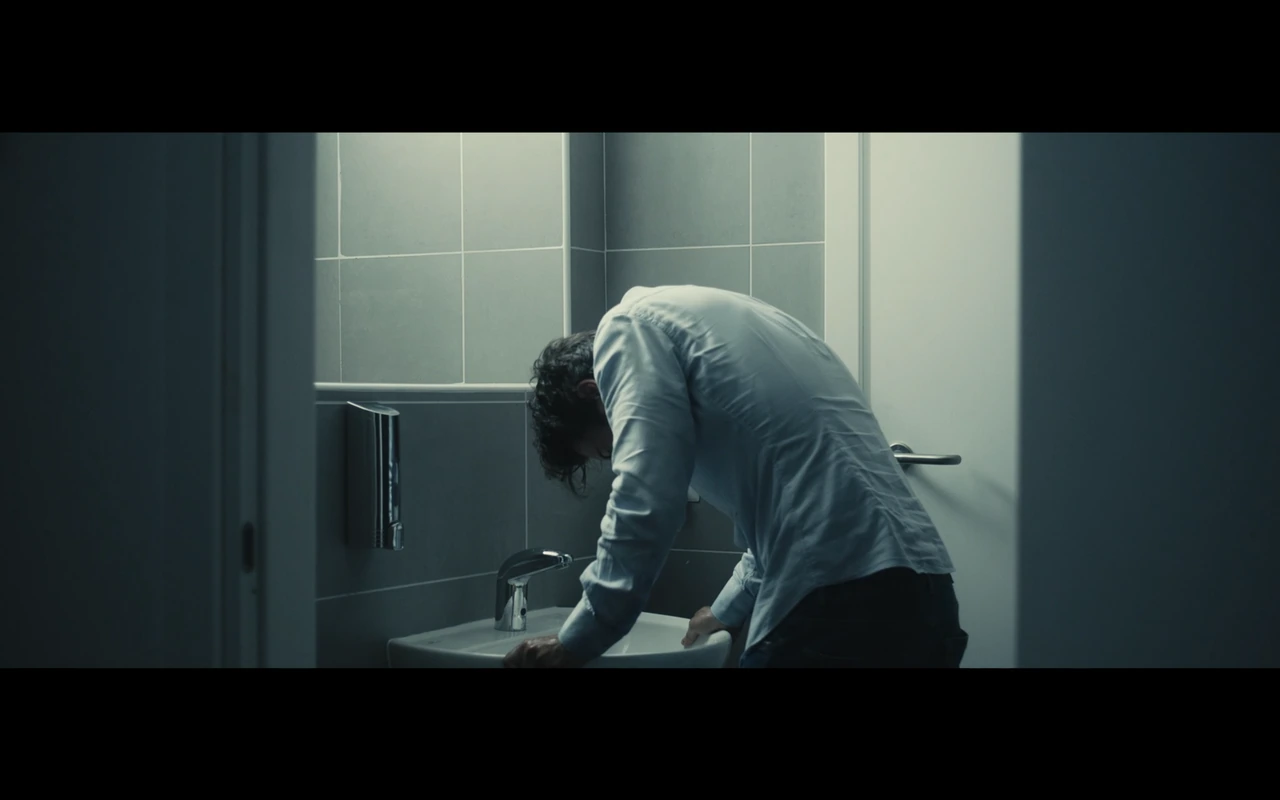 A man leaning over a bathroom sink in cool light