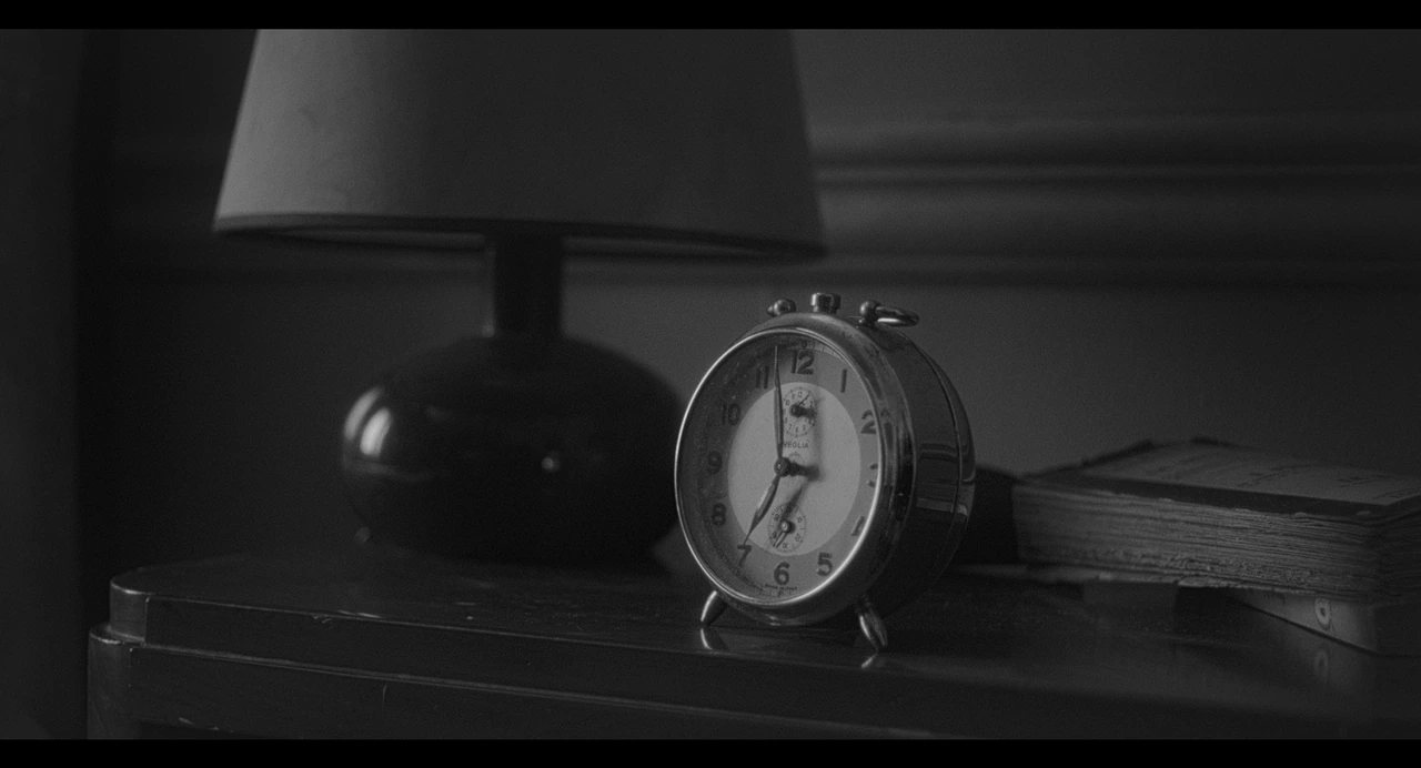 An alarm clock beside a bedside lamp