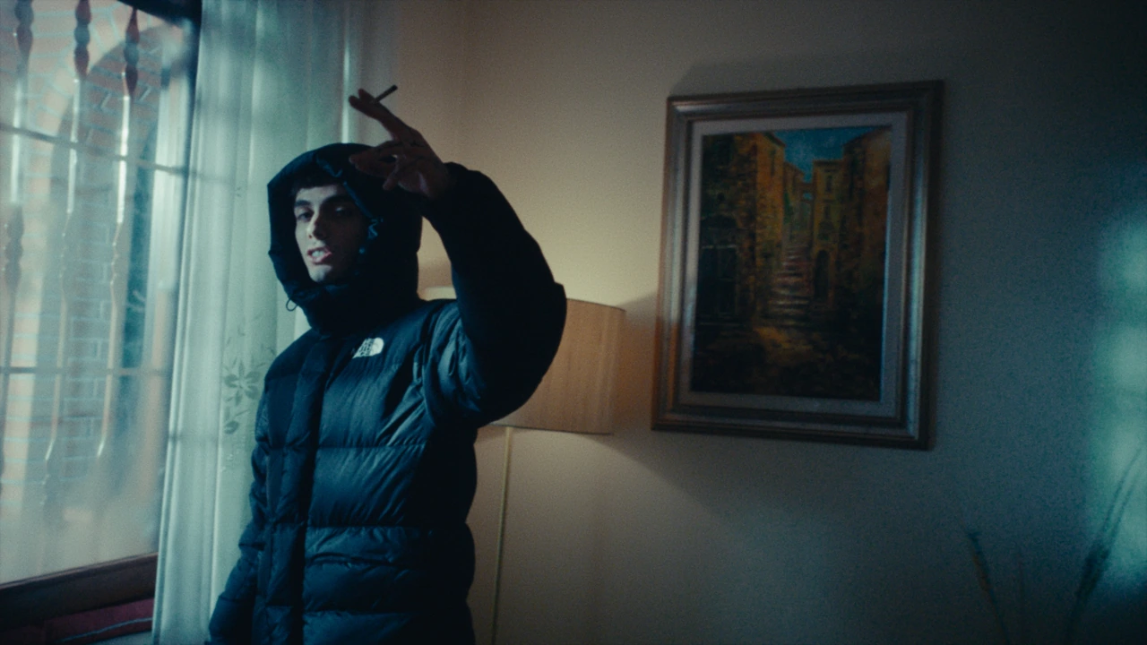 A hooded artist beside a window in blue light