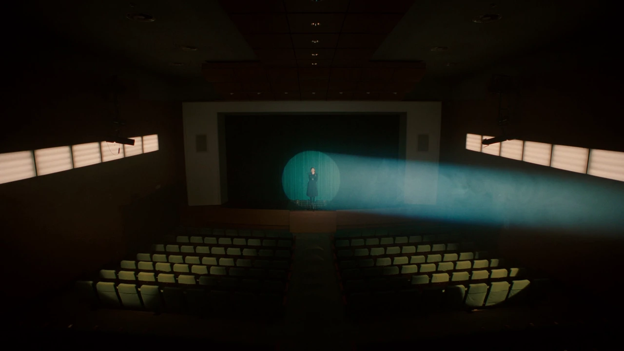 A figure on a theatre stage under a beam of light