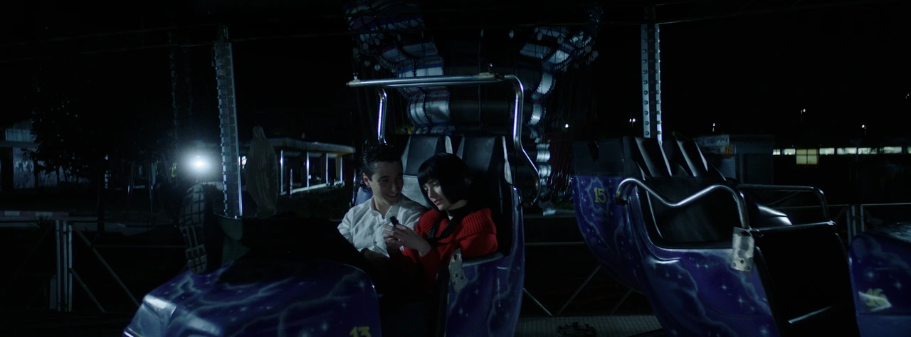 A couple sitting together on a fairground ride at night