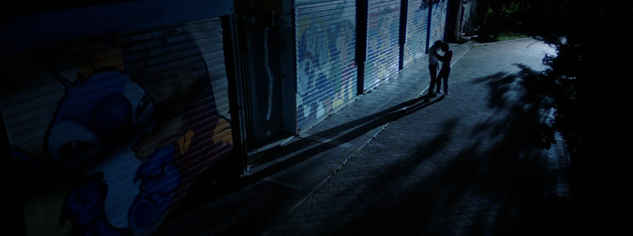 A couple embracing on a blue-lit street at night