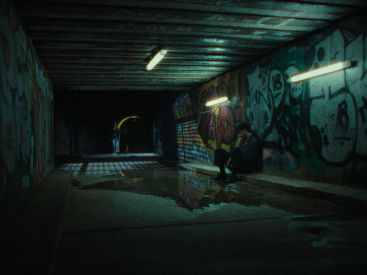 A figure sitting in a fluorescent-lit underpass