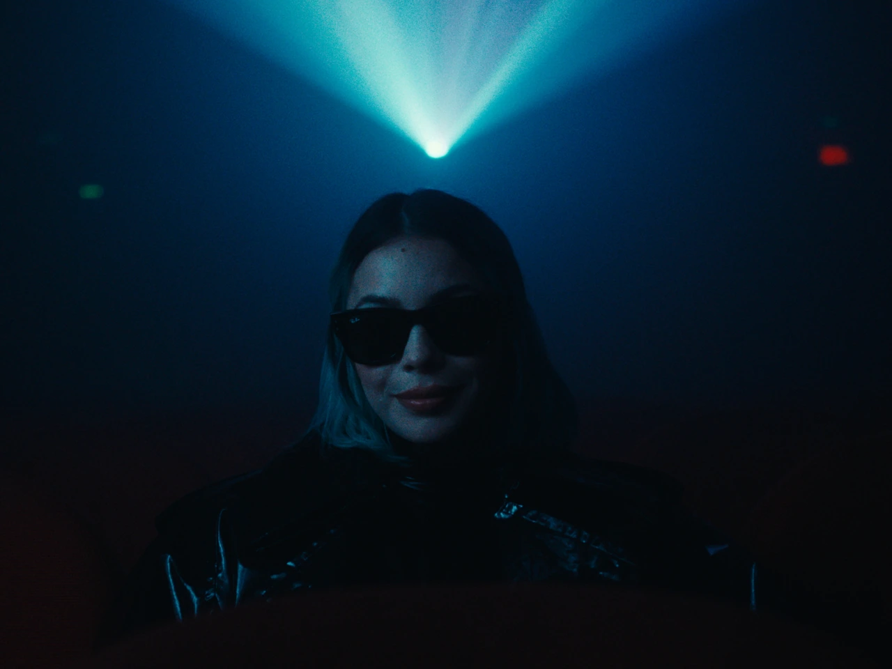 A woman wearing sunglasses beneath a beam of blue light