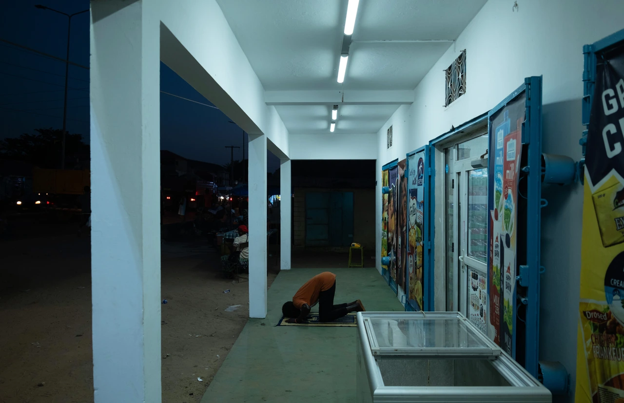 A person praying beneath fluorescent lights outside a shop