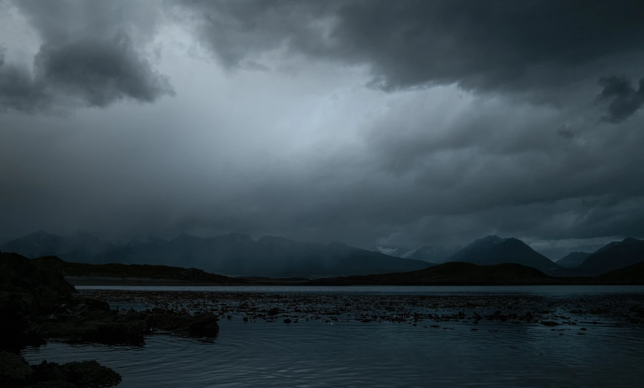 Dark storm clouds over still water and distant mountains