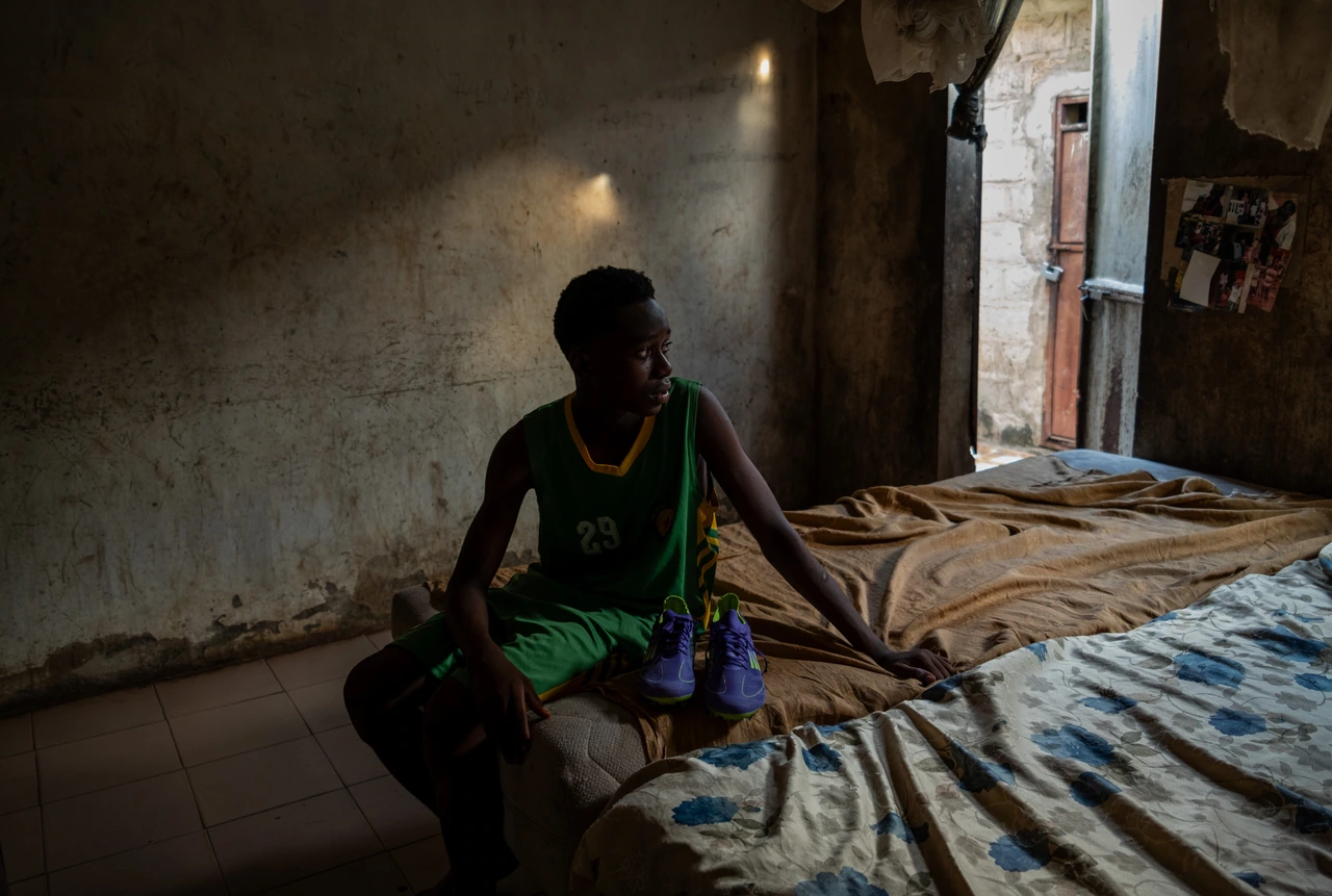 A young person sitting on a bed beside an open doorway