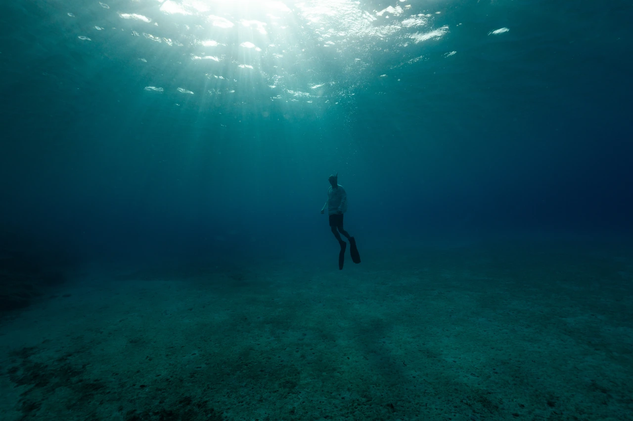 A diver suspended beneath sunbeams underwater